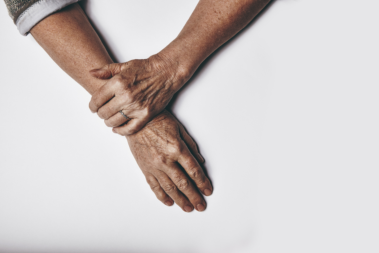 Top view of an elderly woman's hands resting on grey background. Relaxed old female hands together.